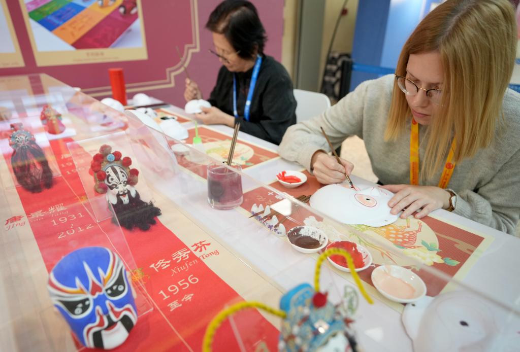 10月16日，在第三屆“一帶一路”國際合作高峰論壇新聞中心，來自比利時(shí)的記者（右）體驗(yàn)畫京劇臉譜。新華社記者 王毓國 攝