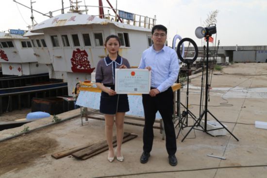 海鮮電商張夢琴與幫辦員手持食品經(jīng)營許可證合影。贛榆區(qū)委宣傳部供圖