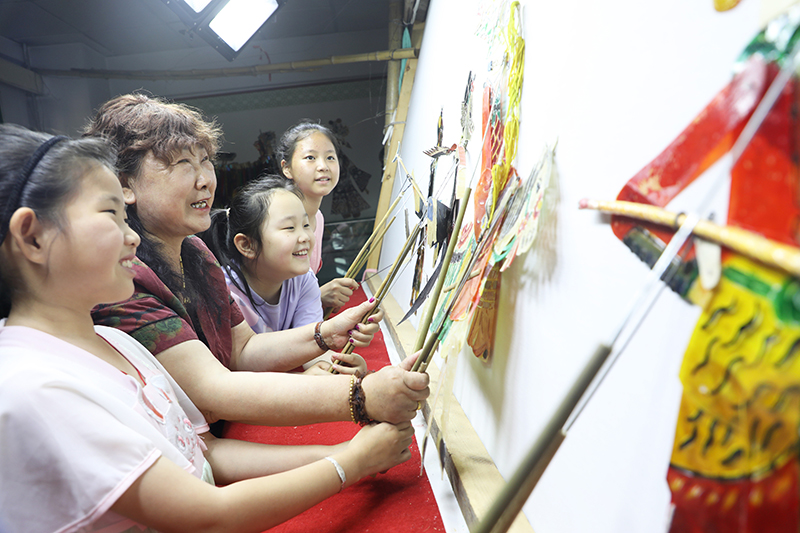 皮影藝人指導(dǎo)小朋友表演皮影戲。