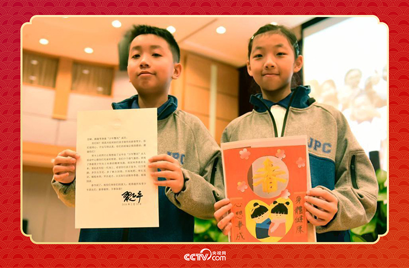 圖為香港“少年警訊”成員郭宏晞（左）展示習(xí)主席回信、羅顥凝（右）展示送給習(xí)主席的賀卡并合影。